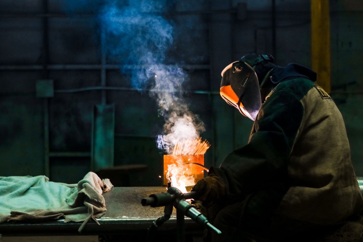 A welder in protective gear standing by finished metalwork
